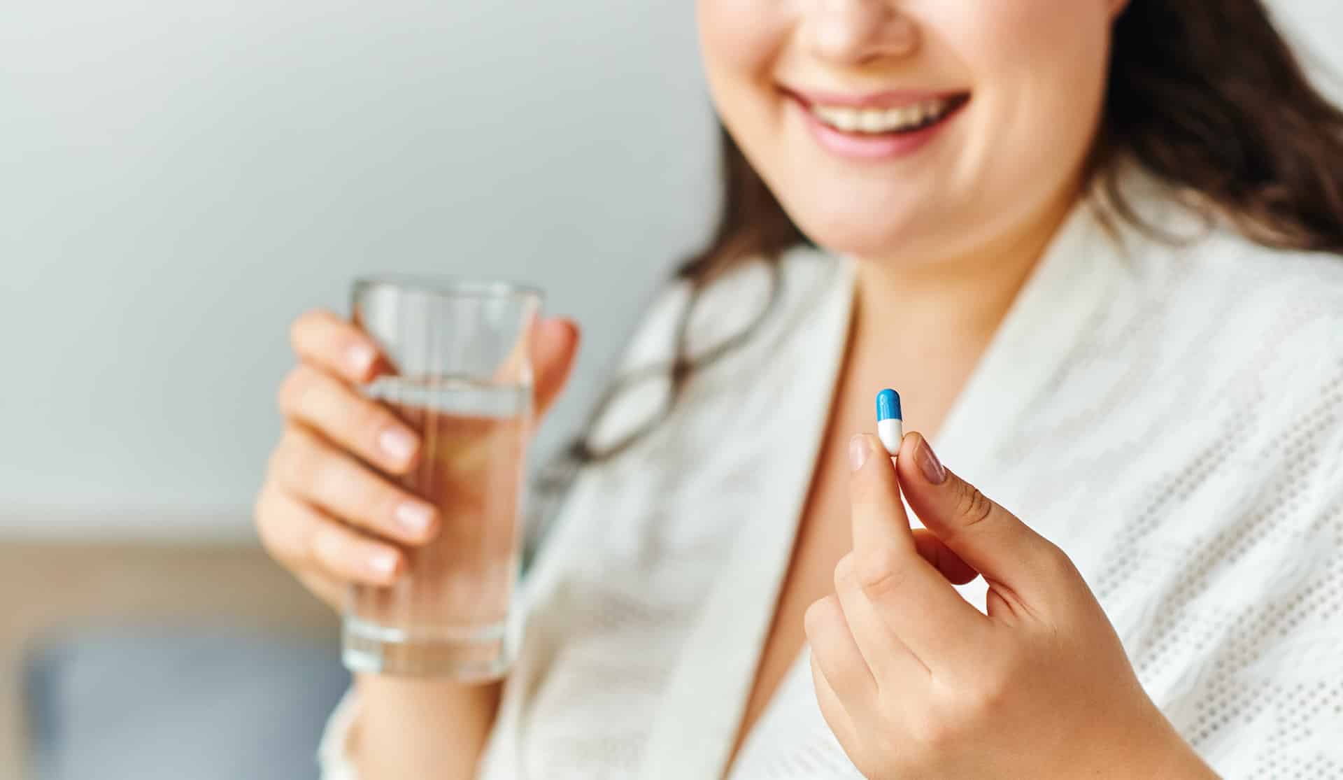 A smiling person holds a blue pill and a glass of water, considering vaping to quit smoking as a healthier lifestyle choice E-Liquid.